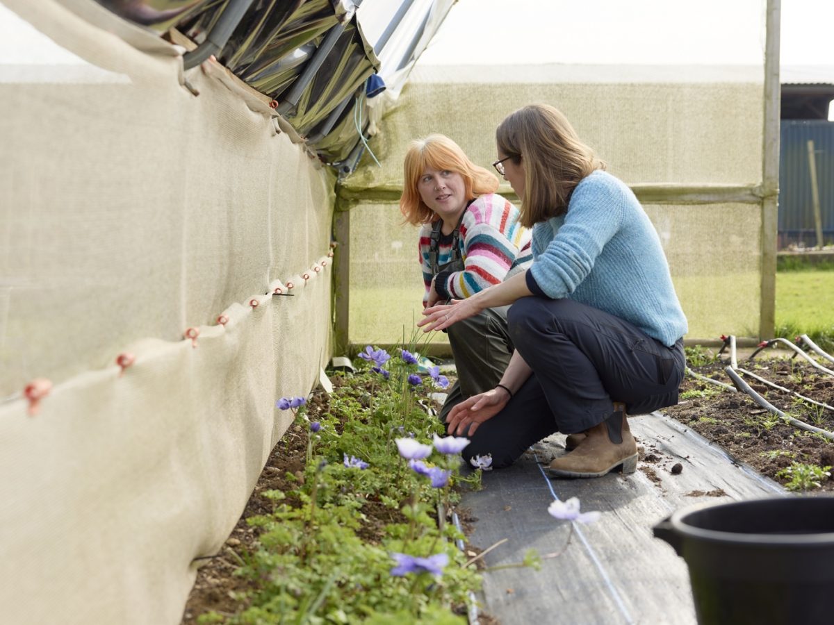 Floristry student Rebecca kneeling in a flower polytunnel with co-owner of Flower & Farmer, Milly Naden-Robinson