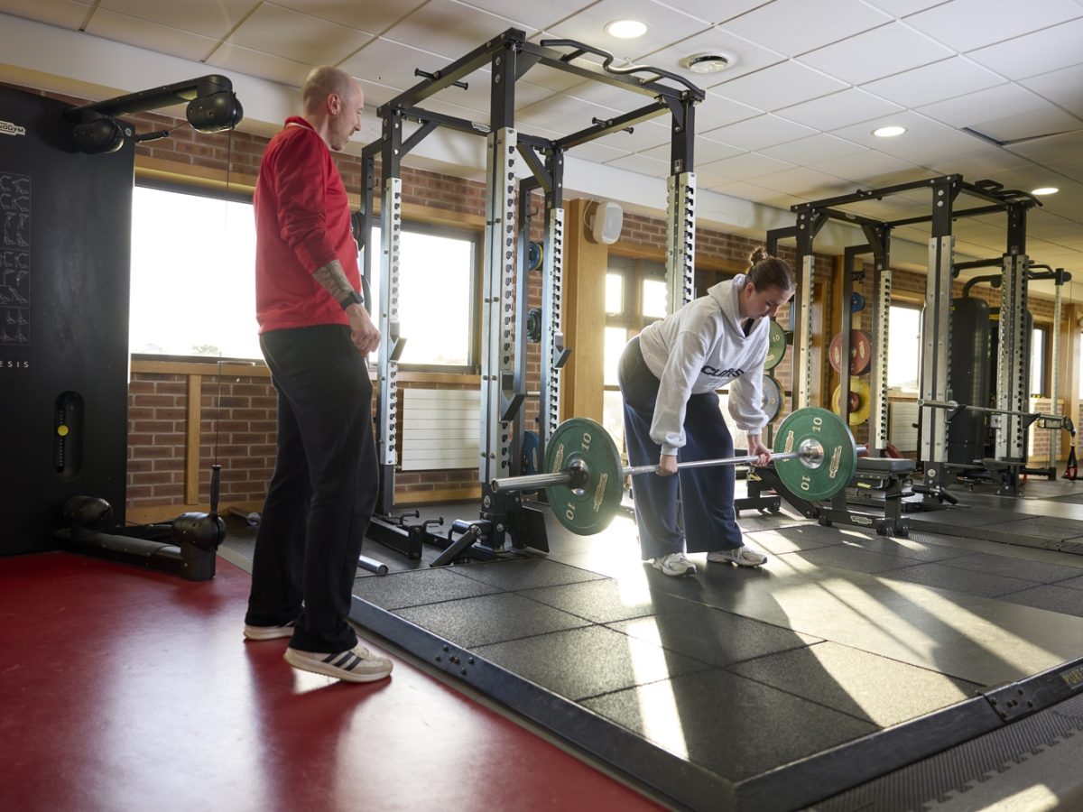 Student lifting weights with coach instructing