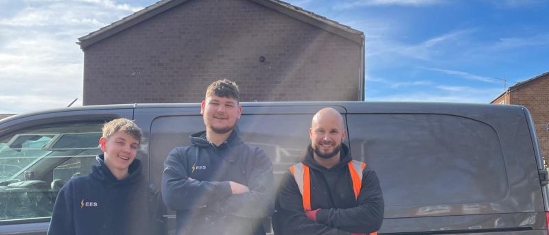 three men standing in front of a grey van