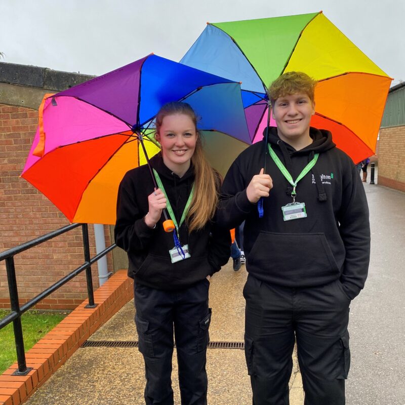 Two uniform public service students holding rainbow colour umbrellas