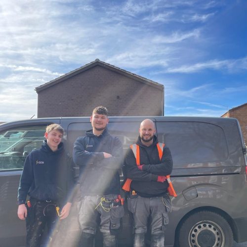 three men standing in front of a grey van